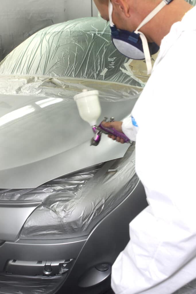 Carrossier masqué appliquant une peinture grise métallisée sur une voiture masquée avec un pistolet DeVilbiss.