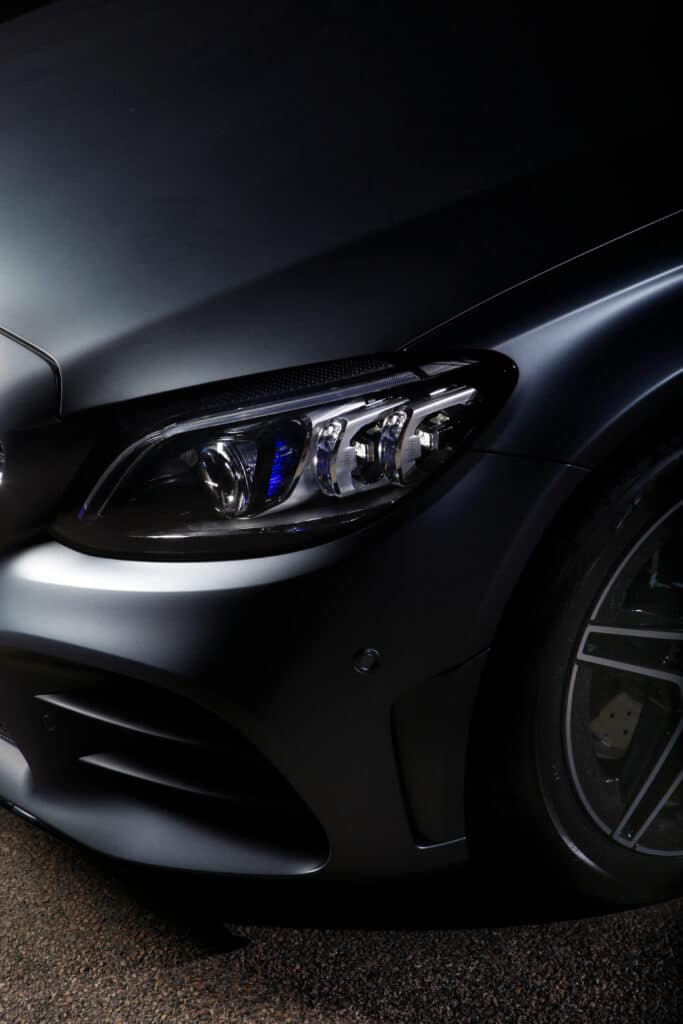 Gros plan sur le phare avant sophistiqué d'une Mercedes-Benz gris mat foncé avec des accents LED bleus et le pneu/jante visible.